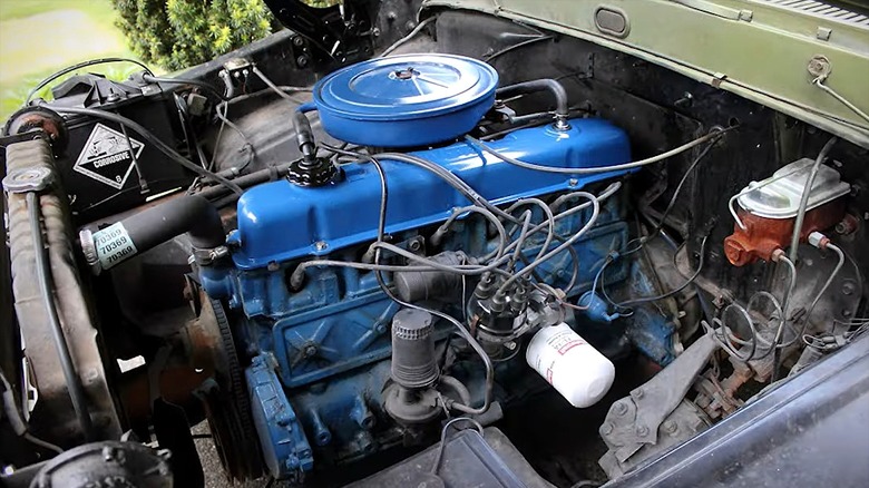 A neatly restored blue Ford 300 inline-six engine mounted in an older pickup truck's bay.