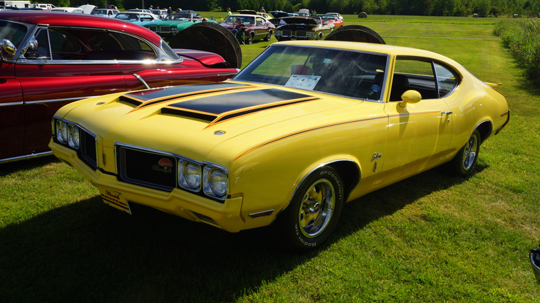 Yellow 1970 Oldsmobile Cutlass Rallye 350 coupe seen from front left parked outdoors at a car show