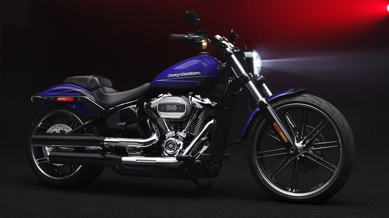 A modern Harley-Davidson bike in metallic blue, dramatically lit in a dark studio with red backlights.