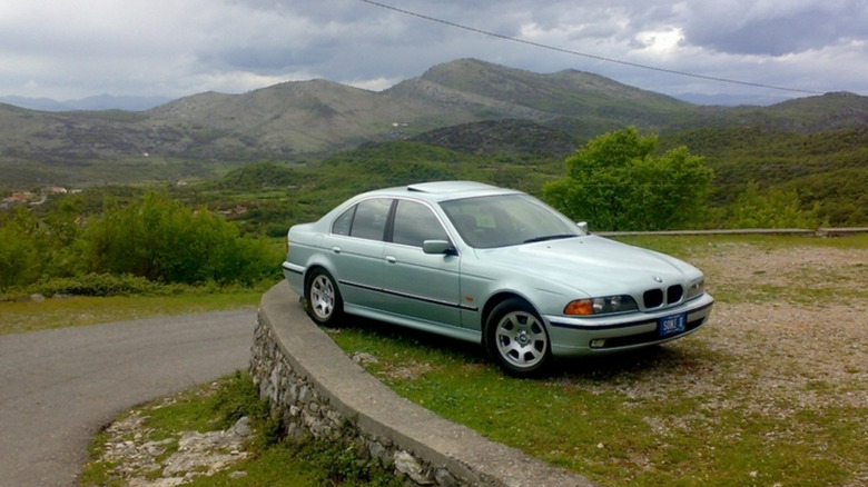 A BMW 5 Series parked on grass, near a road.