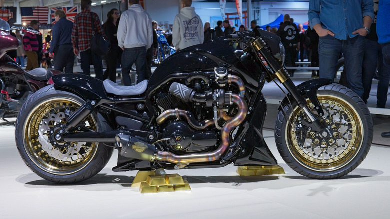 A Harley-Davidson V rod with custom wheels at an expo, being viewed by a crowd