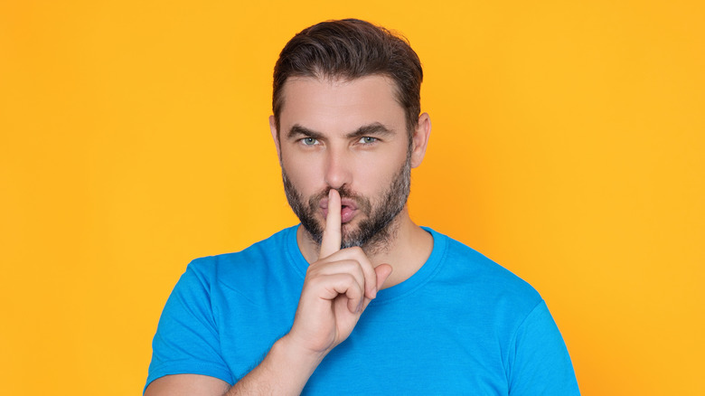 A man shushing at the camera, yellow background.