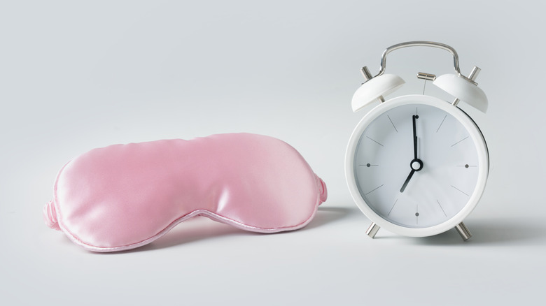 Sleep mask and analog alarm clock on a white surface.