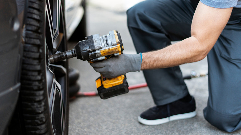A mechanic using a cordless impact wrench on a car tire