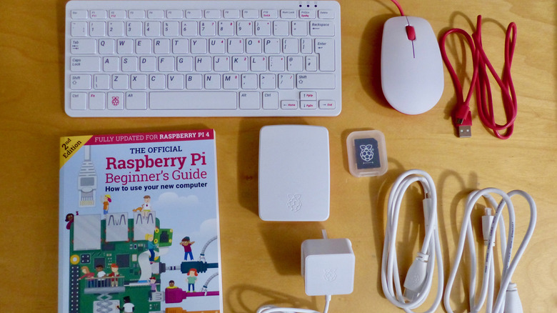 A Raspberry Pi kit laid out on a table with a bunch of cords and a mouse, keyboard, and a book.
