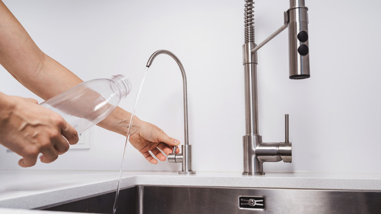 Person's hand using faucet for RO system to fill up plastic water bottle