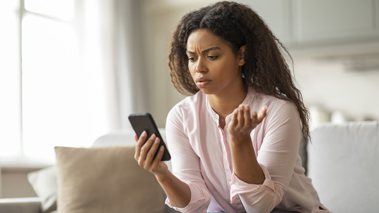 Woman on couch holding smartphone with a concerned look
