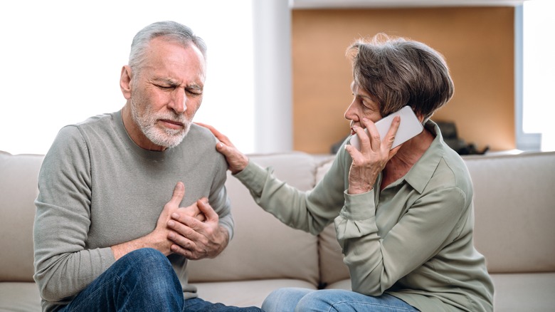 Man on couch with hands to chest while woman talks on smartphone