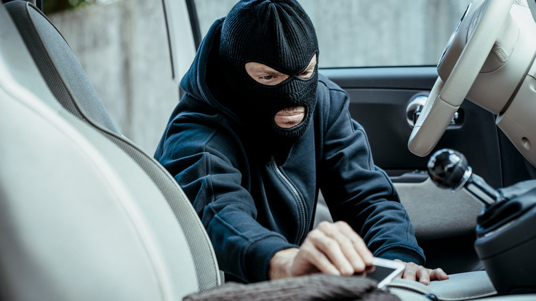 Man in black mask stealing a smartphone from a car