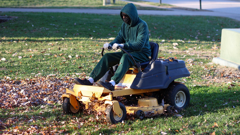 A person in a green hoodie riding a lawn mower