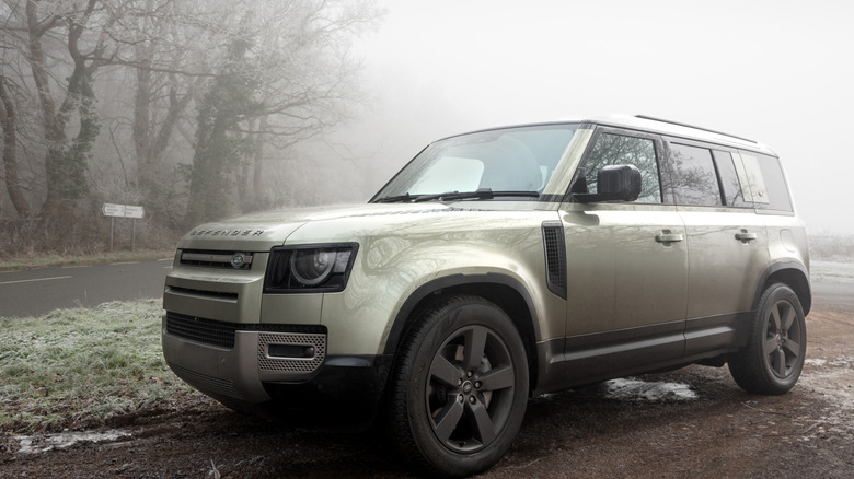 A Land Rover Defender in metallic green paint in a forested area on a foggy day.