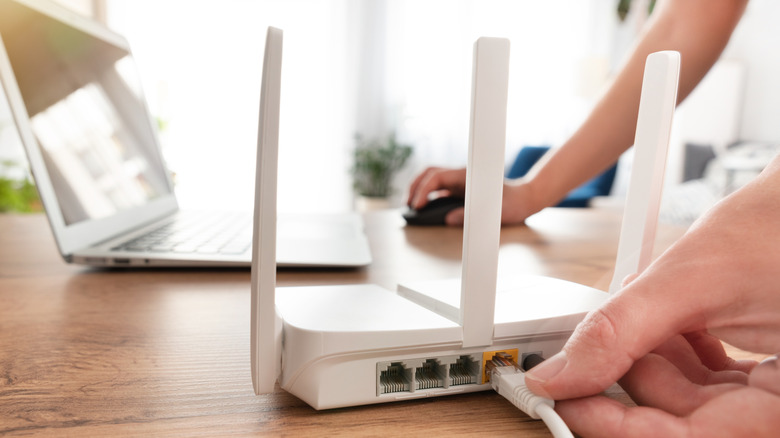 Person connecting modern wi-fi router on light table in living room