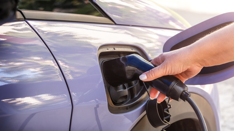 A hand pluggin in the charger on an EV