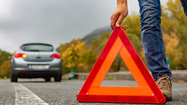 A person placing a reflective triangle behind a vehicle on road.