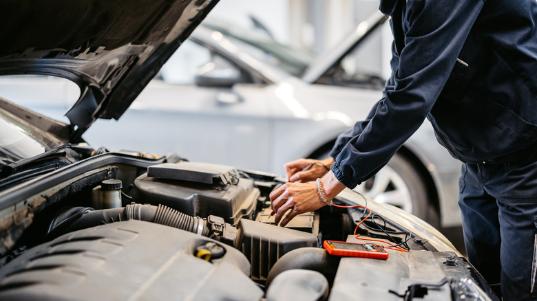 A person holding a measuring device above a car's battery.