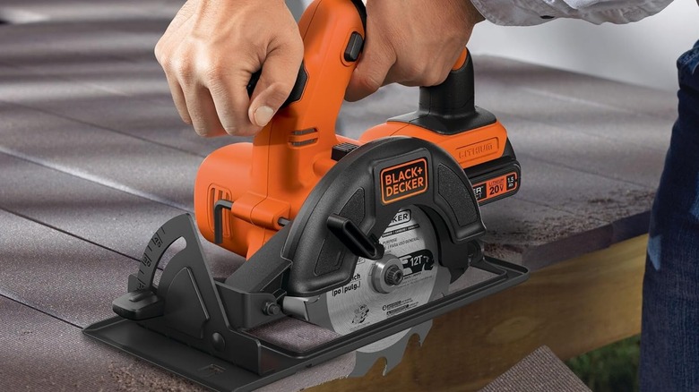 A Black and Decker cordless saw being used on a patio held by a person