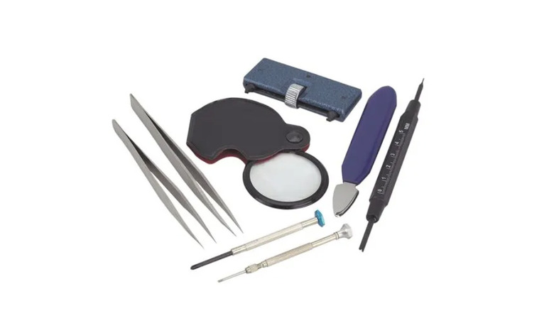 Watch repair kit with two sets of tweezers, two screwdrivers, and other tools against white background