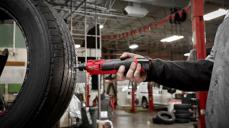 Hand holding Milwaukee tire buffer while drilling tire in workshop
