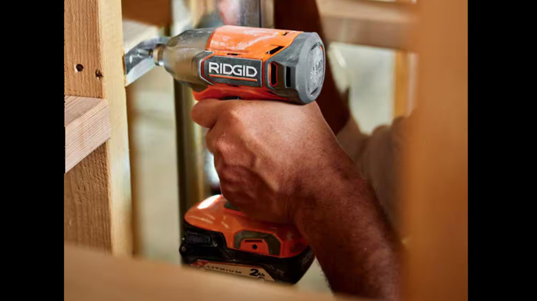 person holding orange impact driver near wall framing