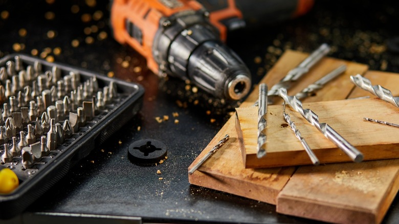 A drill and drill bits sitting on a table with pieces of wood