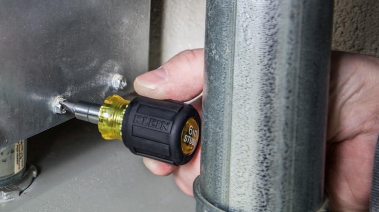 man using yellow stubby screwdriver in a tight space