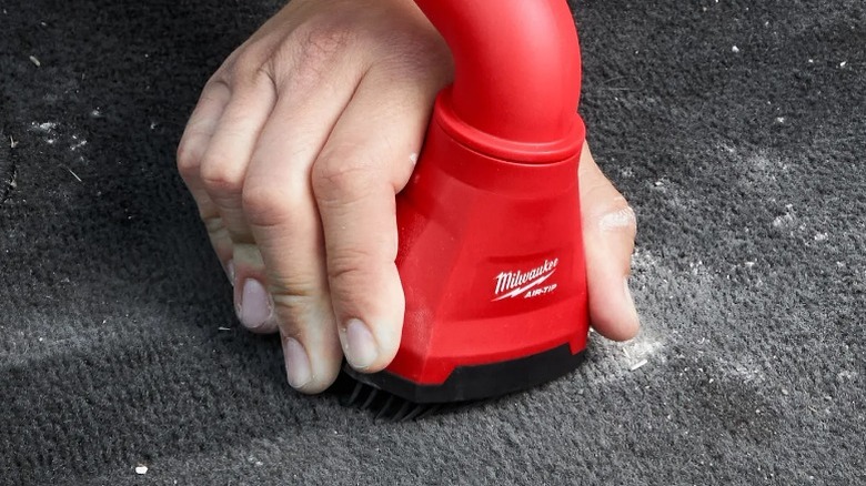 Person using Milwaukee Air-Tip Swiveling Palm Brush to clean carpet