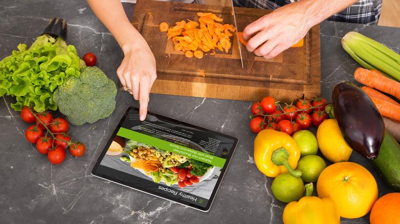 A couple chopping carrot in a chopping board while watching recipe on an iPad