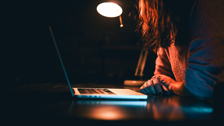 Long-haired person in profile seated at a laptop