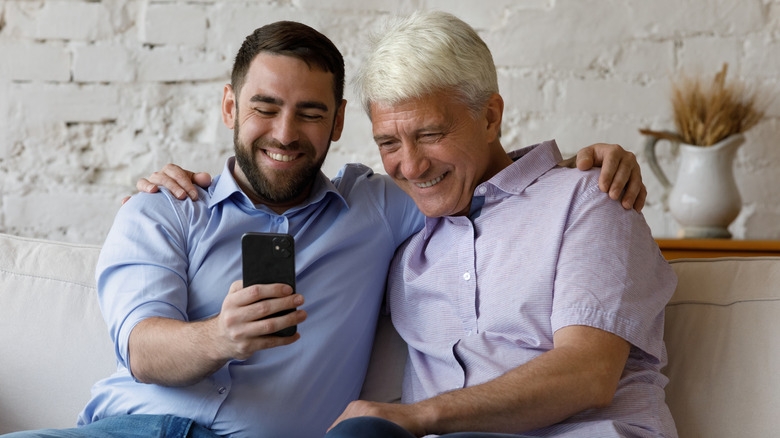 Young and older cheerful men sat looking at an iPhone