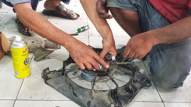 Two people using penetrating oil on rusty vehicle components.
