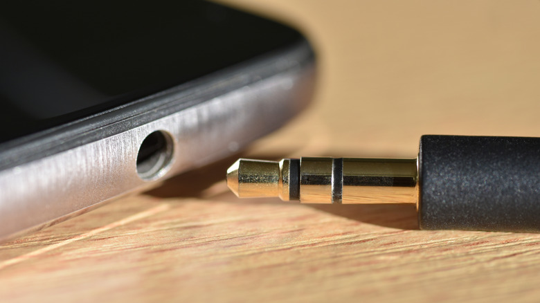 A headphone jack on a smartphone with an auxiliary cable next to it.