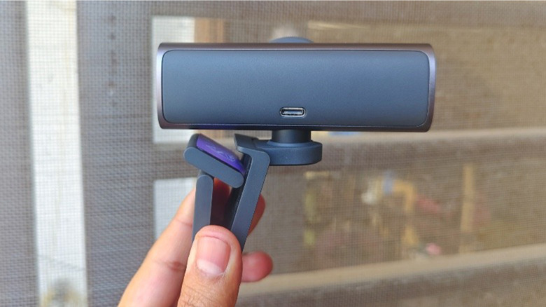 A man holding up a webcam from behind