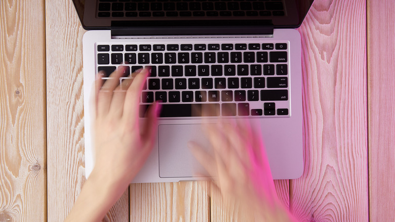 A person typing fast on a laptop keyboard on a table