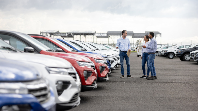 A car salesman showcasing cars to a couple on a dealership lot.