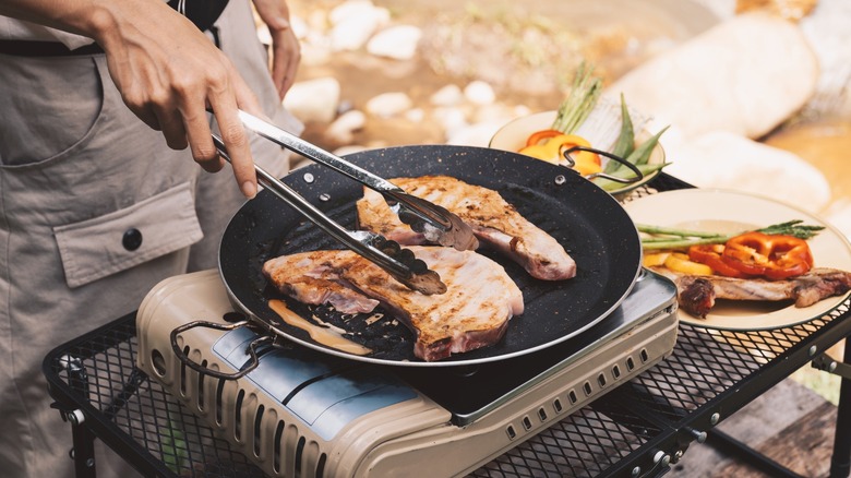 Person cooking meat on a camping stove