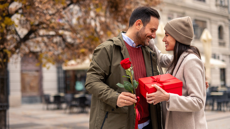 couple smiling while holding rose and box
