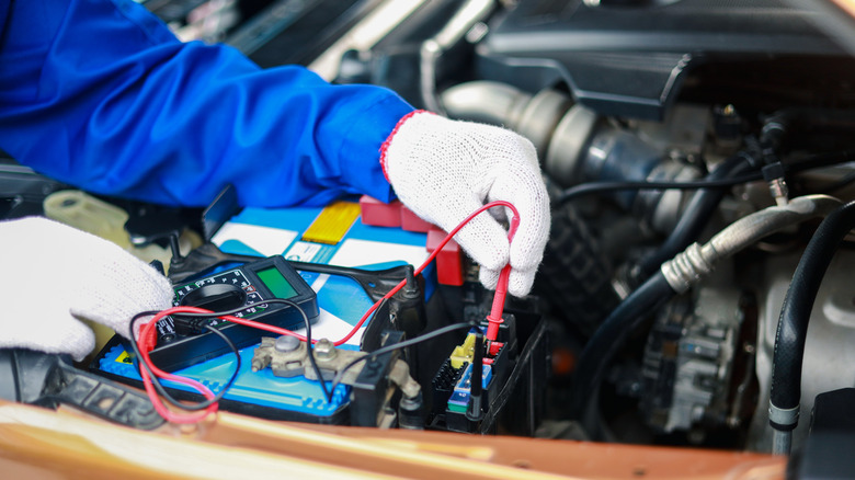 A person wearing gloves using multimeter on vehicle's battery
