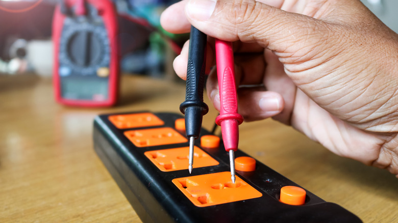 A person multimeter testing continuity on an extension cord