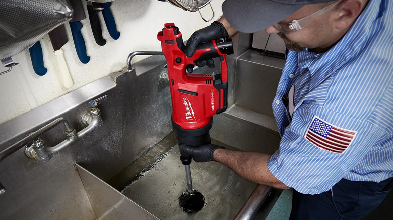 Man cleaning sink drain with air gun