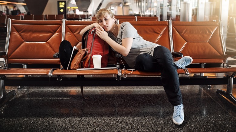 A woman sleeping, leaning on her bag, in an airport's boarding lounge.