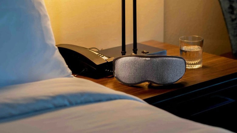 The Lumos sleeping mask sitting on a cabinet, next to a bed.