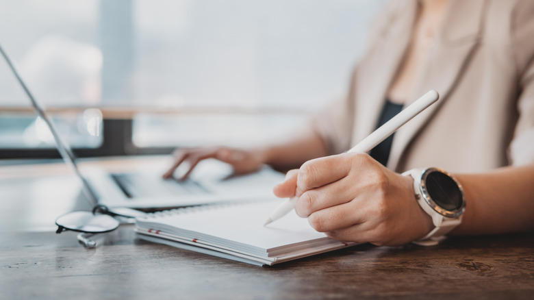 Worker using a pen, paper, and laptop