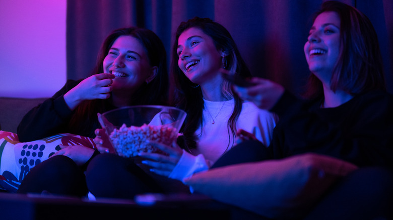 Three women watching movies and eating popcorn in the living room.