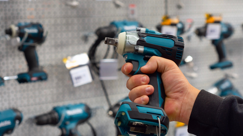 A hand holding a power drill in front of a large display of drills.