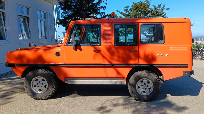 Bright orange Amphiranger amphibious 4x4 vehicle parked outside a building, showcasing its rugged design and all-terrain capabilities.