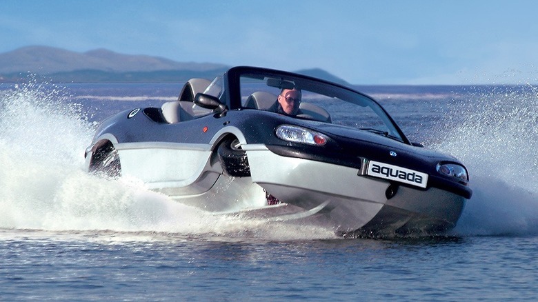 Gibbs Aquada amphibious car driving on water with man at the wheel, showcasing land-to-water transformation capabilities.