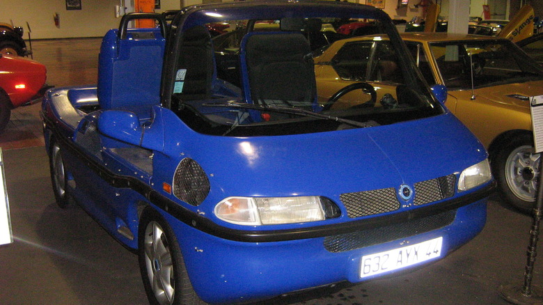 A blue Hobbycar B-612 in its convertible specification, four seats, front-left three quarters view visible inside an auto museum.