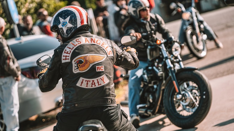A Hells Angel biker on a classic cruiser motorcycle, back visible, turning their head.