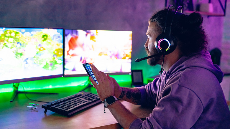 Person wearing headphones and using at a smartphone while sitting at a desk with two monitors.