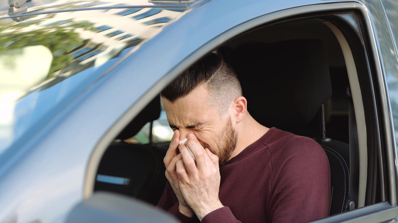 Man sneezing inside his car